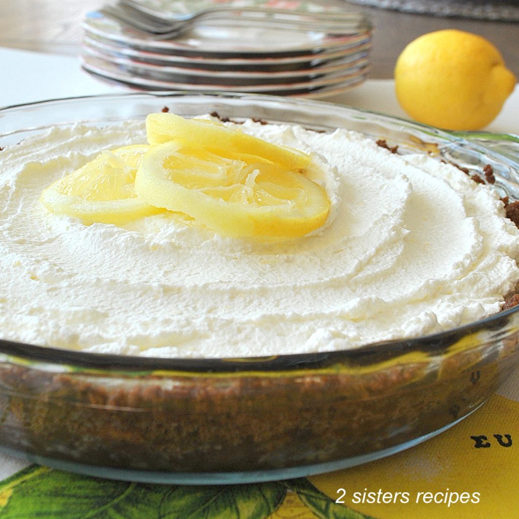 A side view of the lemon cream pie on the table with a set of plates and forks behind it.