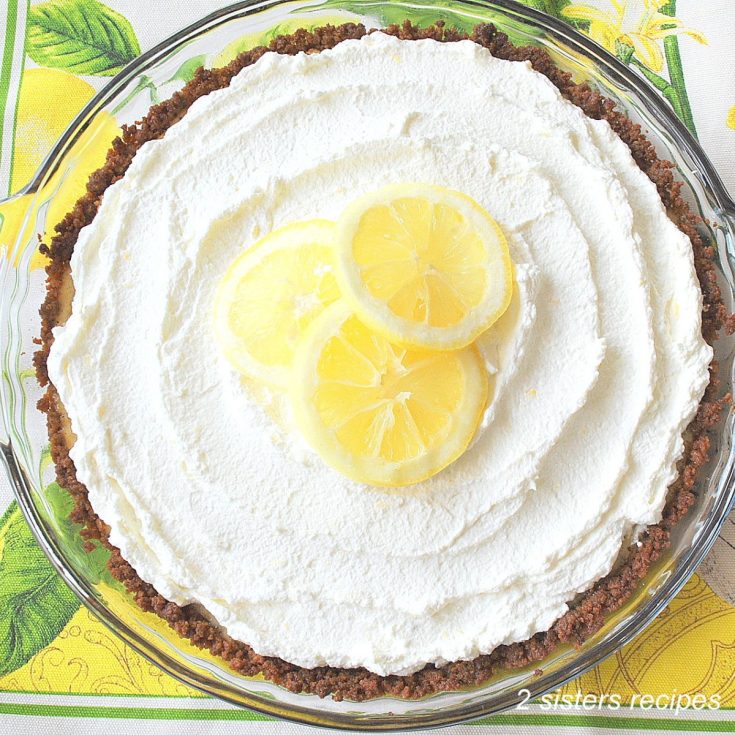 A lemon pie topped with whipped cream and 3 lemon slices on top.