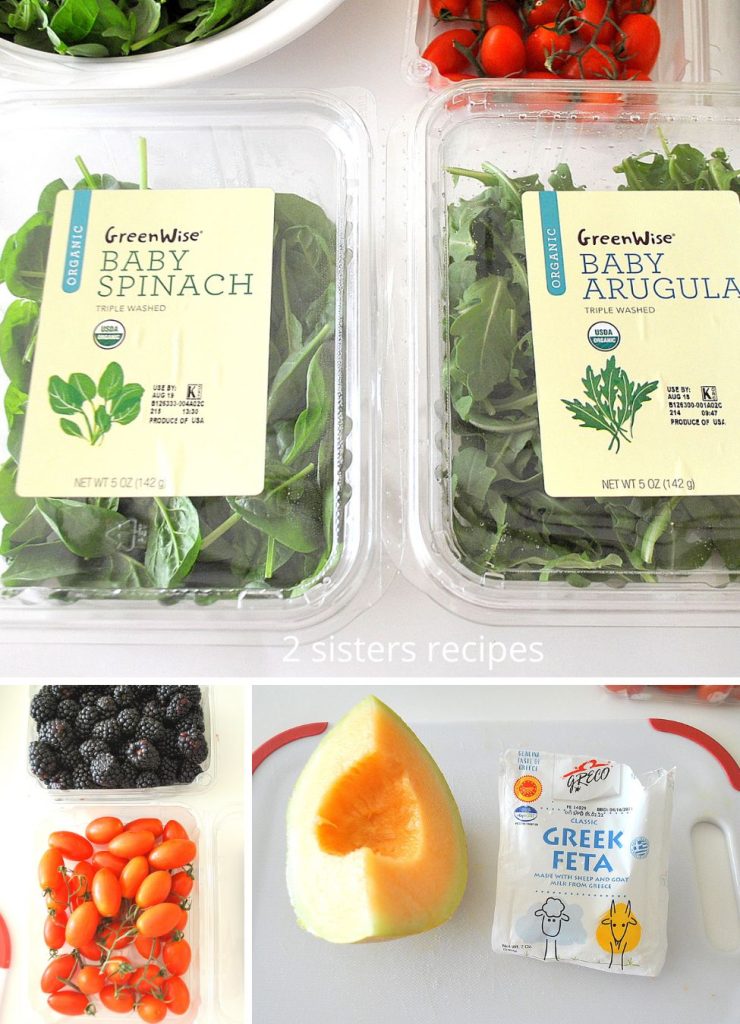 Packages of prewashed greens. plus a wedge of cantaloupe, fresh blackberries and cherry tomatoes and feta cheese are placed on the table.