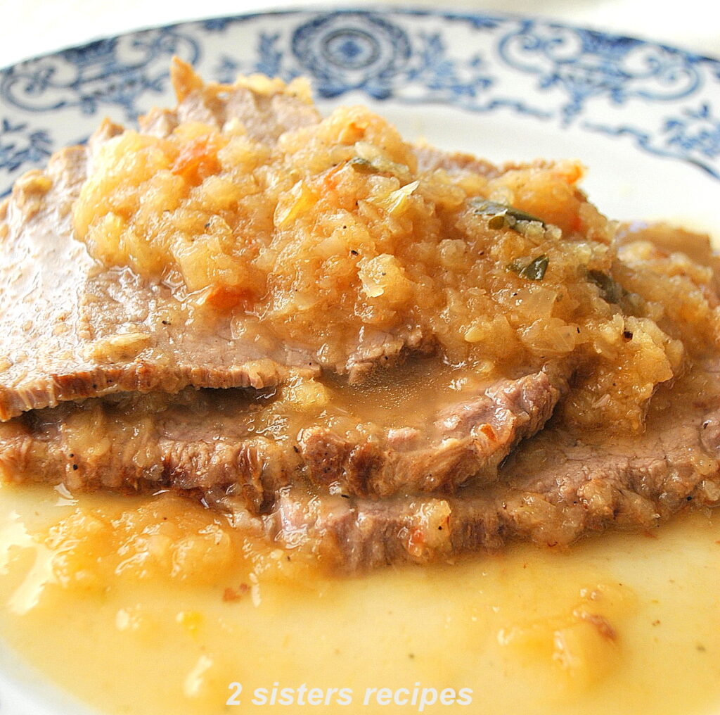 Sliced meat topped with caramelized onions and served on a dinner plate.