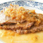 Sliced meat topped with caramelized onions and served on a dinner plate.