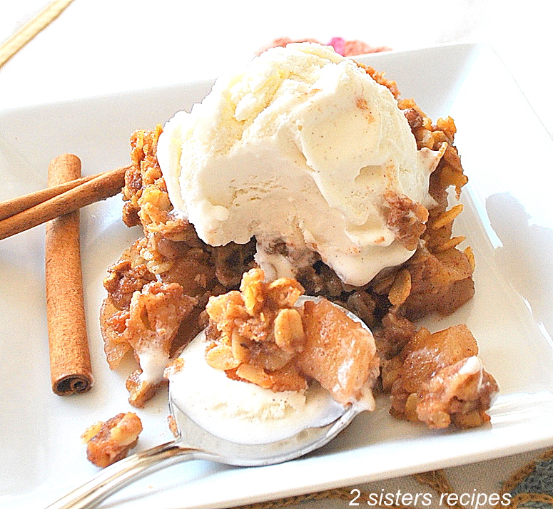 A white plate with apple crumble with scoop of vanilla ice cream on top. by 2sistersrecipes.com