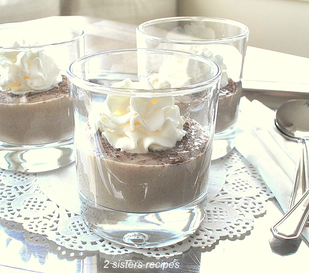 Three glasses filled with pudding and topped with whipped cream served on a silver tray.