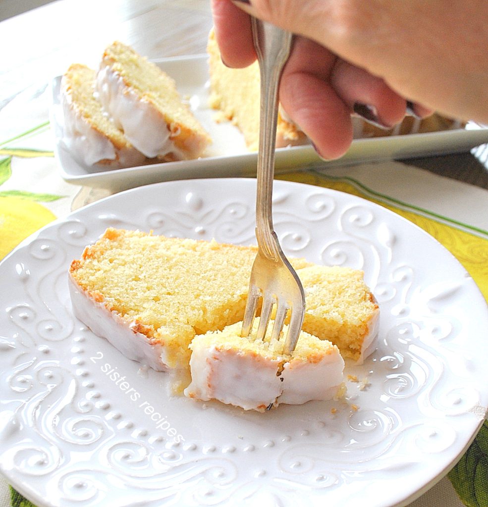A fork into a slice of cake on a white plate. by 2sistersrecipes.com