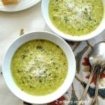 Two white bowls filled with a pureed broccoli and parmesan soup.