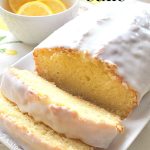 A lemon cake topped with white glaze, and sliced, and served on a white platter.