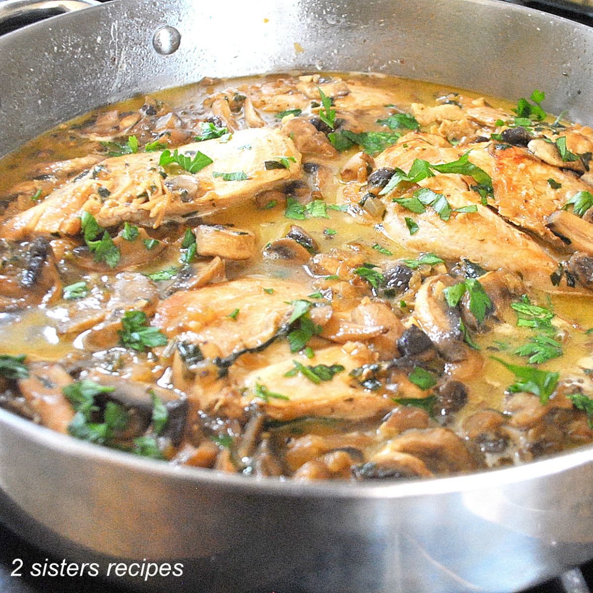 A large silver skillet loaded with chicken and mushrooms and parsley.