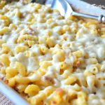 A white baking dish filled with elbow pasta and melted cheese on top with a large spoon on the side.