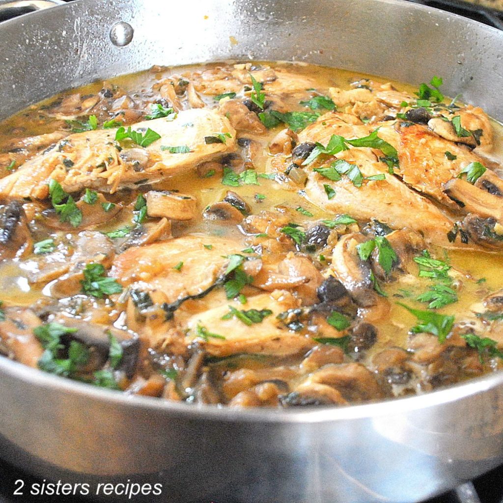 A large skillet filled with pieces of chicken, sauce and fresh parsley scattered on top