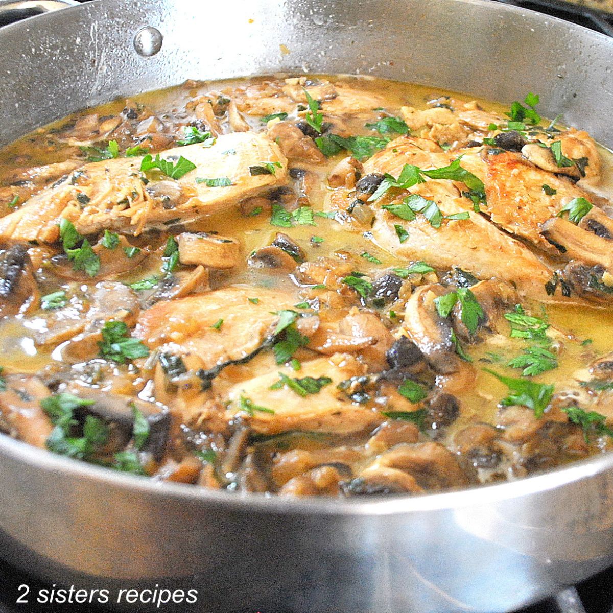 A large skillet filled with pieces of chicken, sauce and fresh parsley scattered on top