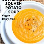 A white bowl and plate with a serving of a thick creamy orange colored soup with black pepper on top.