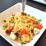 A fork twirled inside the center of the spaghetti in a white square bowl.