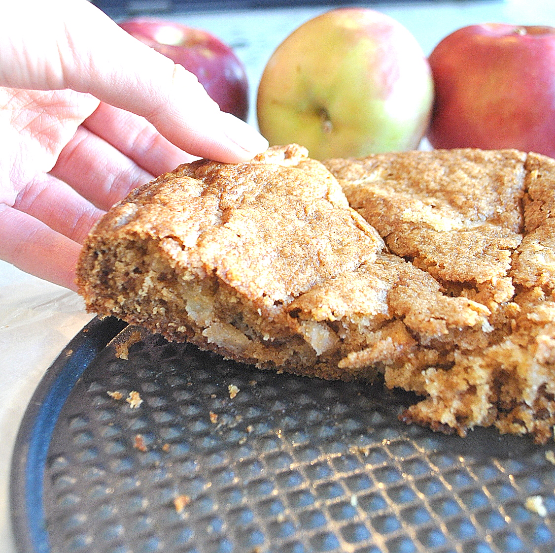 a hand taking a slice of apple blondie from the round cake pan.