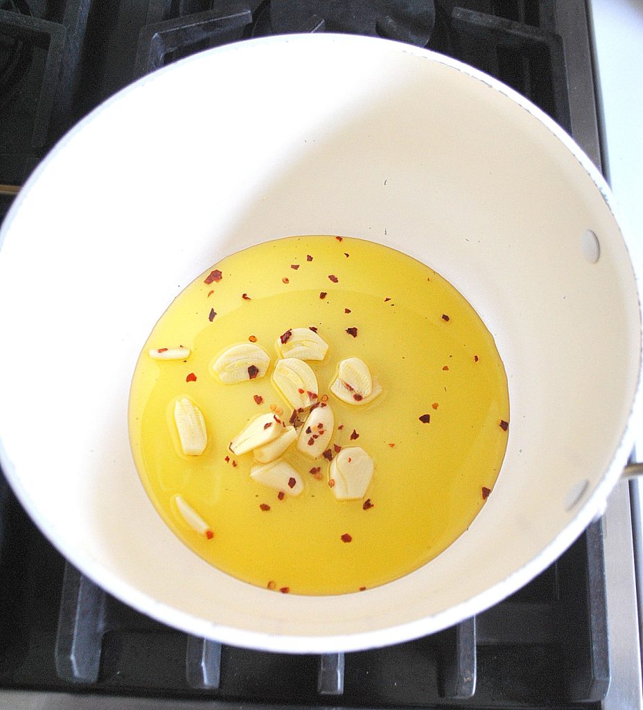 A white pot with olive oil, garlic and crushed red pepper. by 2sistersrecipes.com