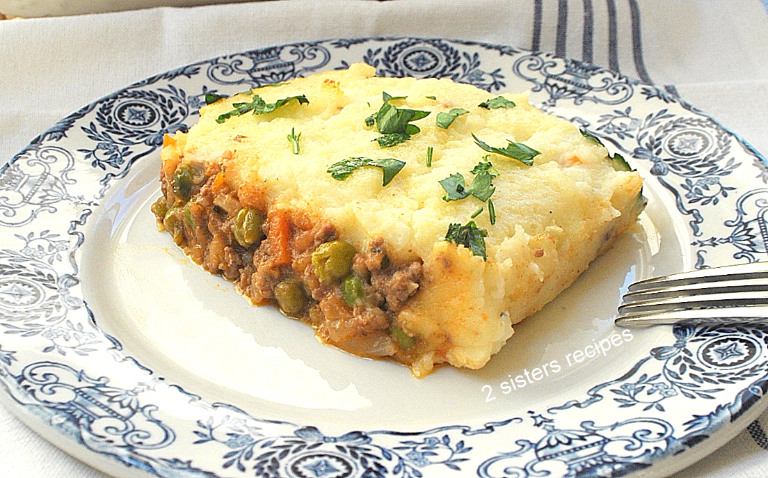 A blue and white plate with a serving of casserole with meat and peas and mashed potatoes on top.