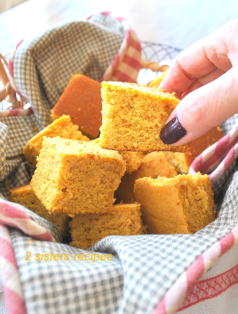 A hand holding a piece of cornbread. by 2sistersrecipes.com