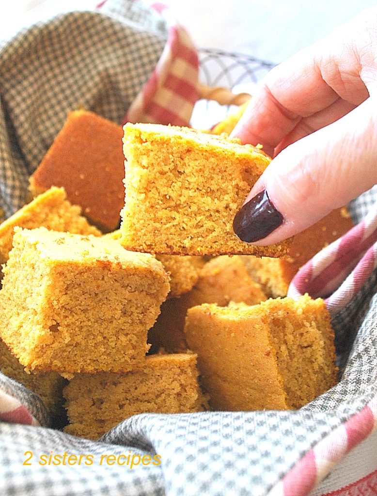 A hand holding a piece of cornbread. by 2sistersrecipes.com