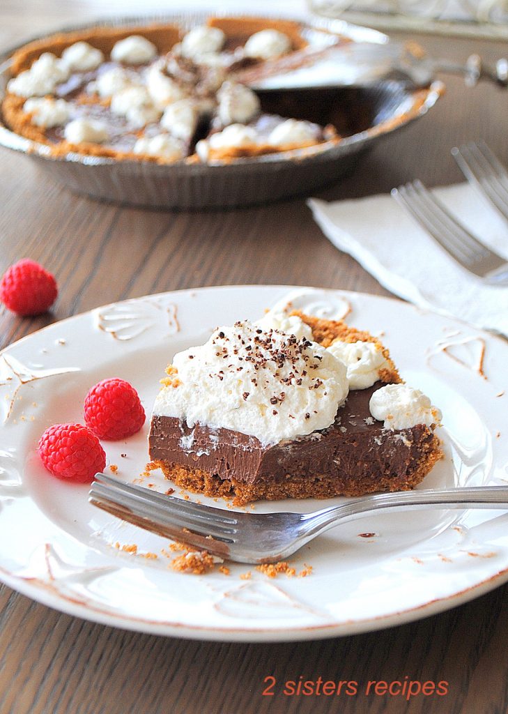 A slice of silky chocolate cream pie on a white plate with a fork. by 2sistersrecipes.com