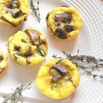 Mini egg frittatas are set on a white plate with fresh thyme sprigs scattered on the plate.