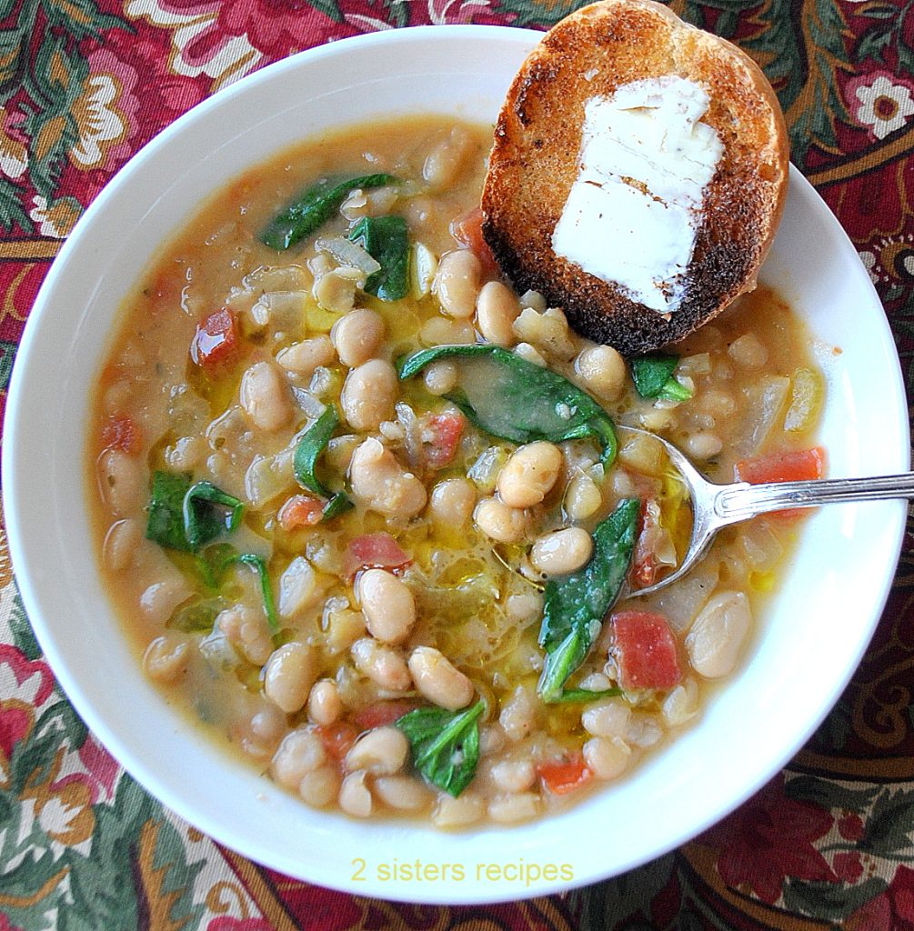 Brothy White Beans Soup is loaded with tomatoes and spinach in a white bowl with spoon and toasted bread with butter.