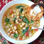 A bowl of soup loaded with white beans, spinach and a slice of toasty bread.