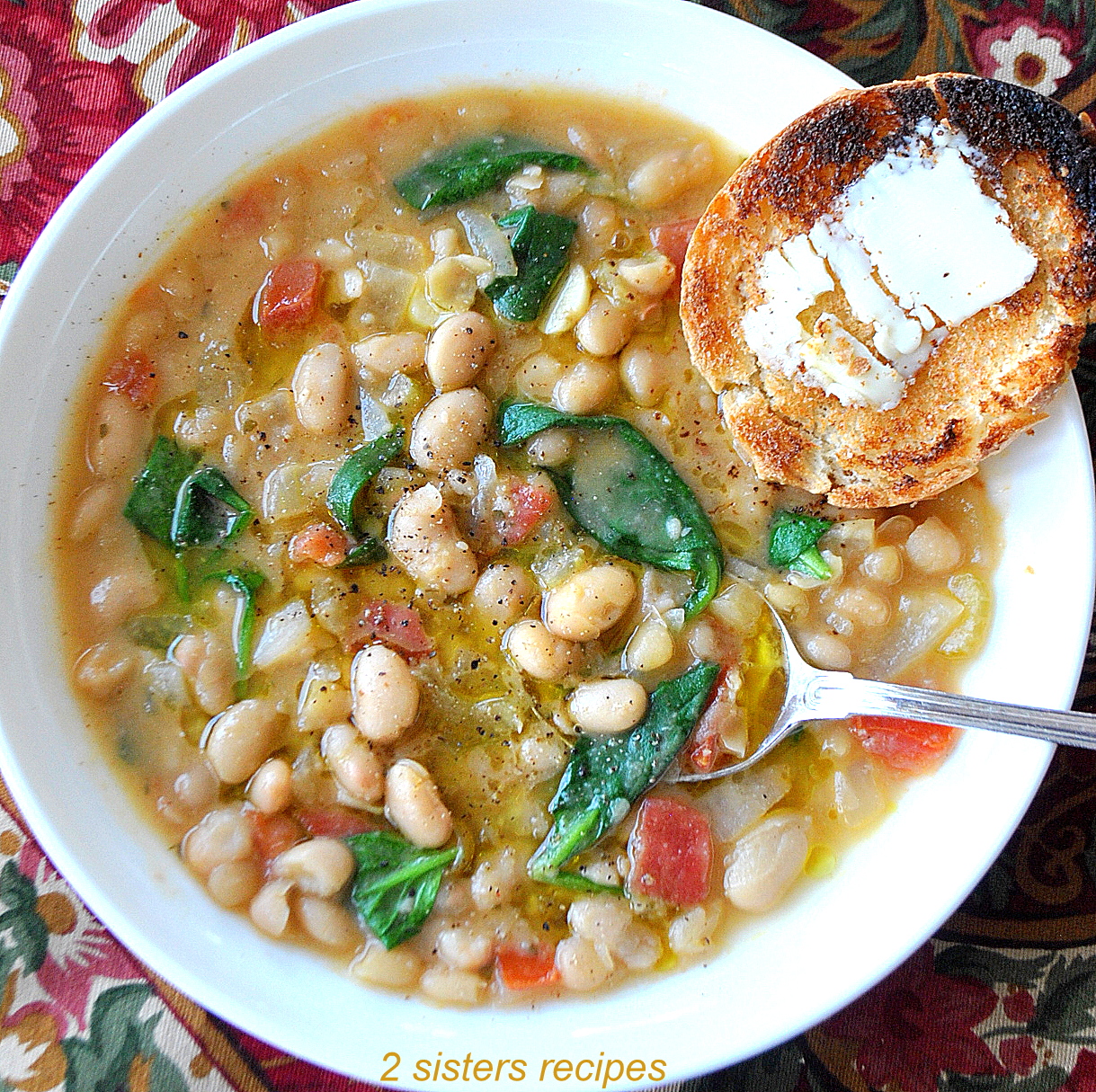 A bowl of soup loaded with white beans, spinach and a slice of toasty bread.