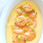 A oval platter filled with creamy polenta and cooked shrimp on top.