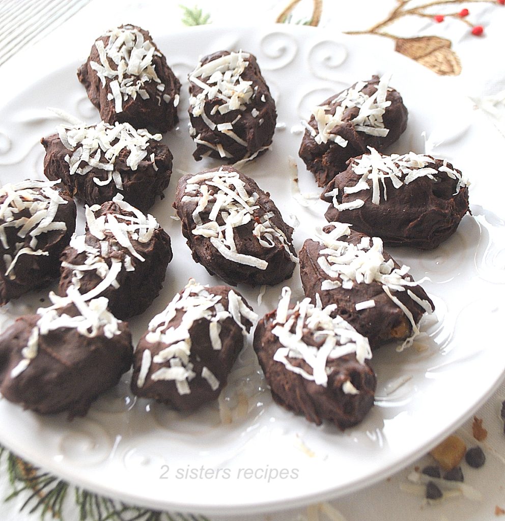 A white dish with chocolate covered dates on it. 