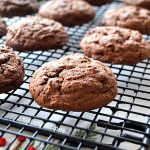 A wire rack filled with baked double chocolate chip cookies.