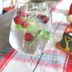A wine glass filled with a cocktail, fresh cranberries and mint as garnish.