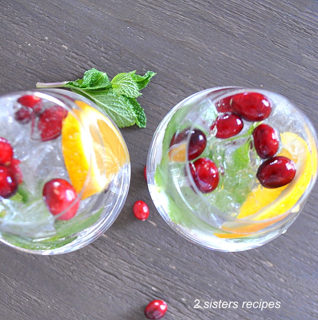 2 glassed filled with cranberries, mint and a slice of orange. by 2sistersrecipes.com