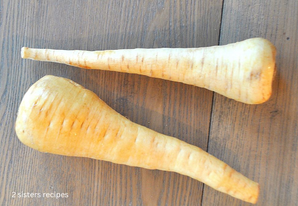 A photo of 2 fresh parsnips on a wooden table. by 2sistersrecipes.com