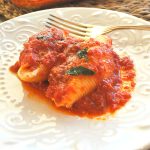 Two stuffed shells covered with tomato sauce on a white plate.