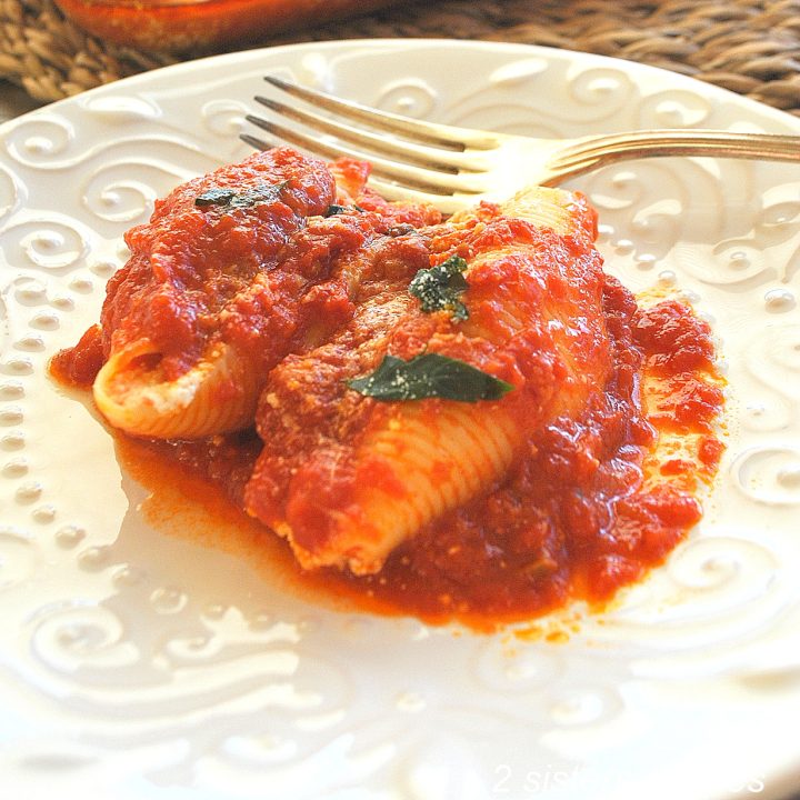Two stuffed shells covered with tomato sauce on a white plate.