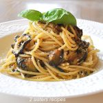 A white plate with a serving of spaghetti and thin slices of zucchini, topped with fresh basil leaves.