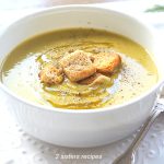 A white bowl filled with split pea soup with some croutons on top.