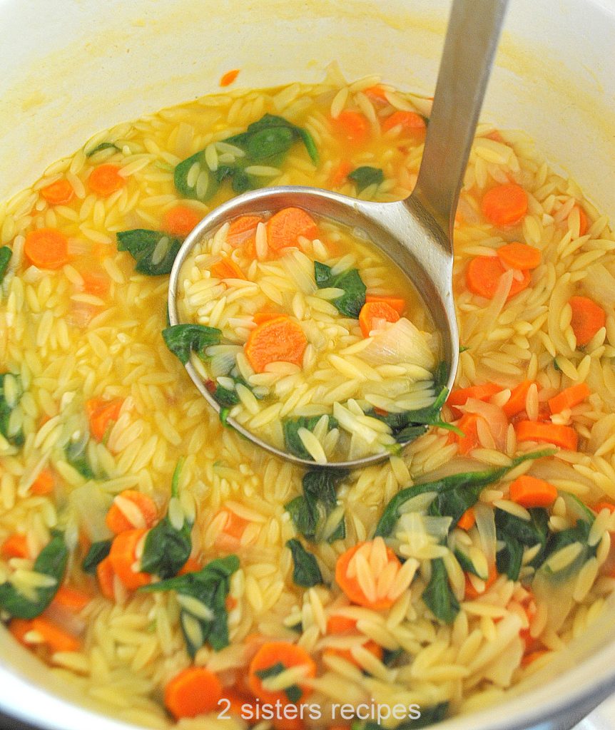 A soup ladle filled with lemon orzo soup in a pot. by 2sistersrecipes.com