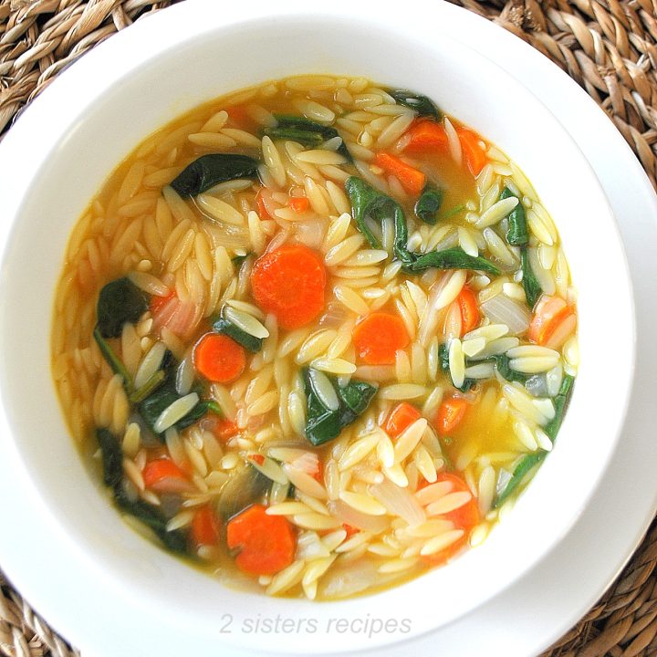A white bowl filled with an orzo soup loaded with carrots and spinach.