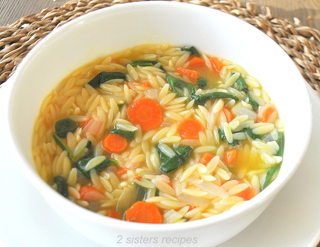 A white bowl filled with orzo soup, with veggies. by 2sistersrecipes.com