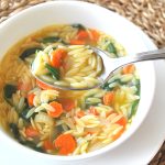 A spoonful of lemon orzo soup over a white bowl.