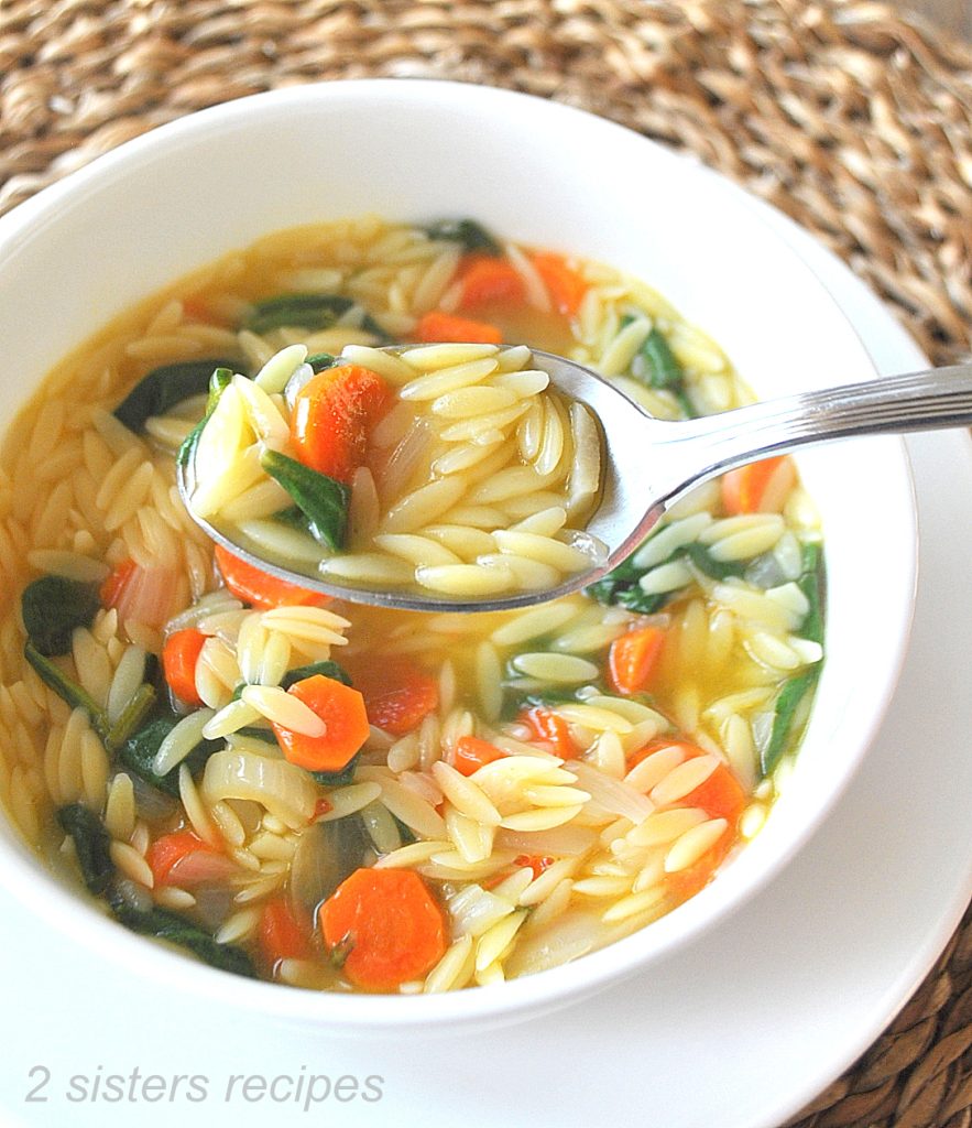 A spoonful of lemon orzo soup over a white bowl. by 2sistersrecipes.com