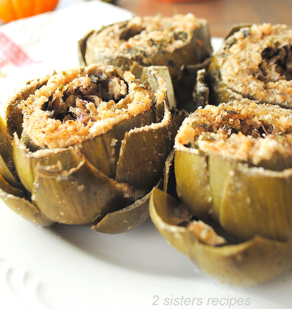 A white plate with four stuffed artichokes topped with breadcrumbs.