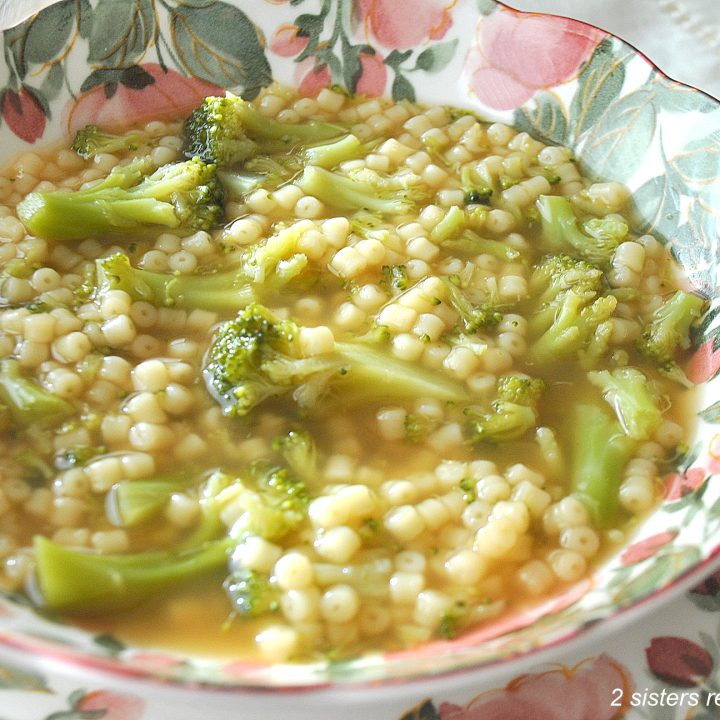 A pink and green bowl of soup with broccoli florets and little pasta.