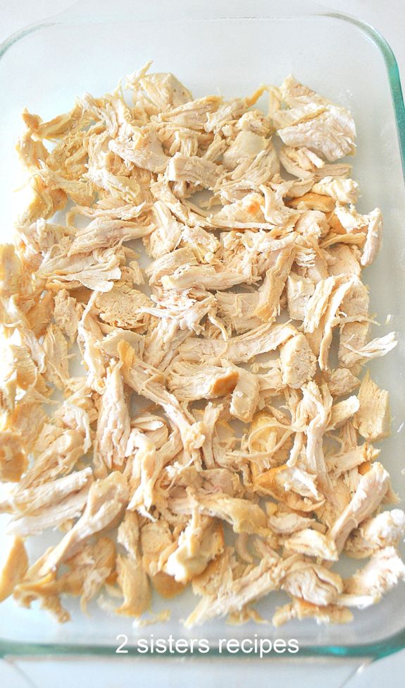 Shredded cooked chicken laid in a casserole dish by 2sistersrecipes.com