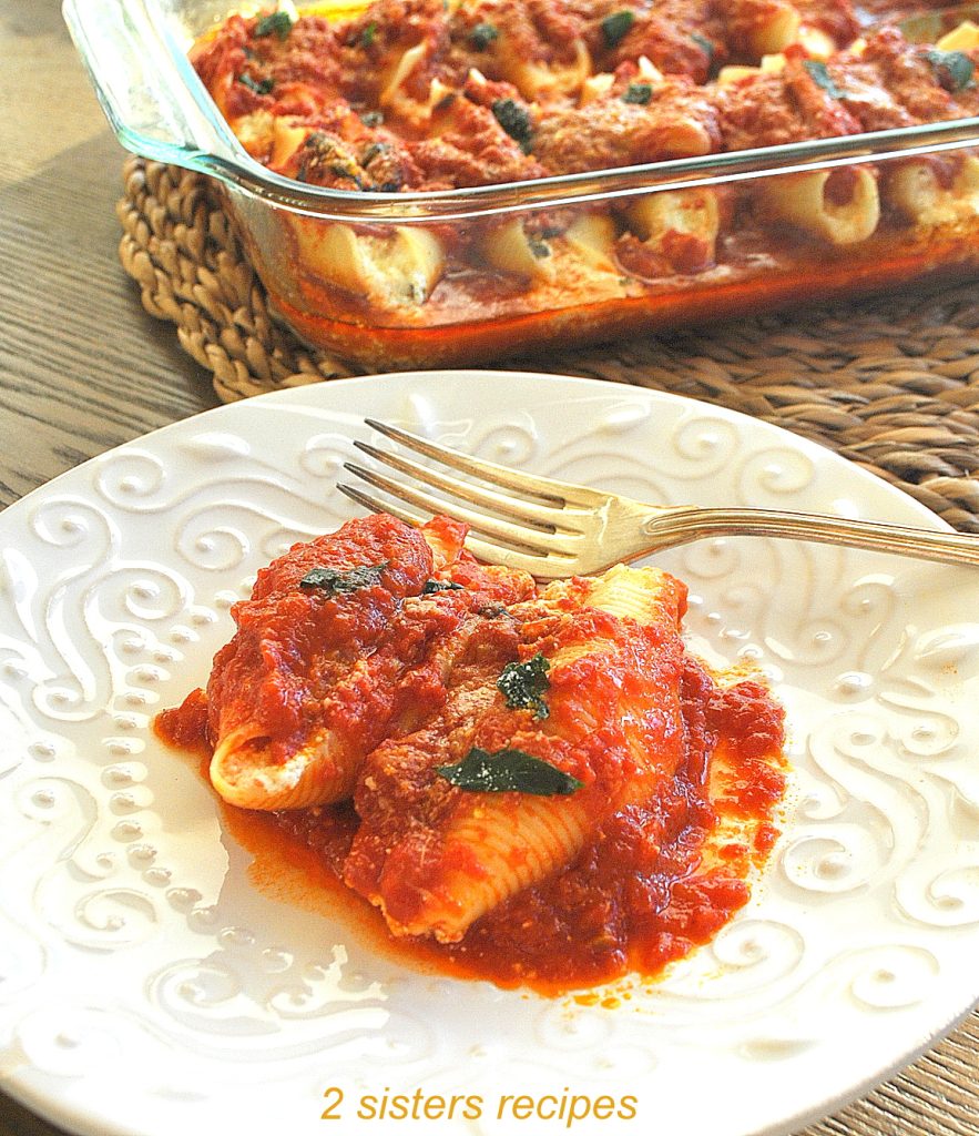 A white plate with 2 stuffed shells with sauce, and a fork. by 2sistersrecipes.com