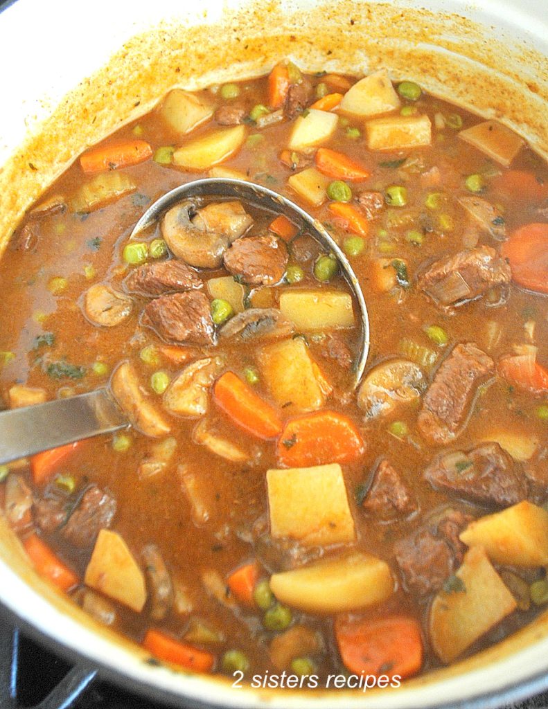 A ladle over a large pot filled with the beef vegetable soup.