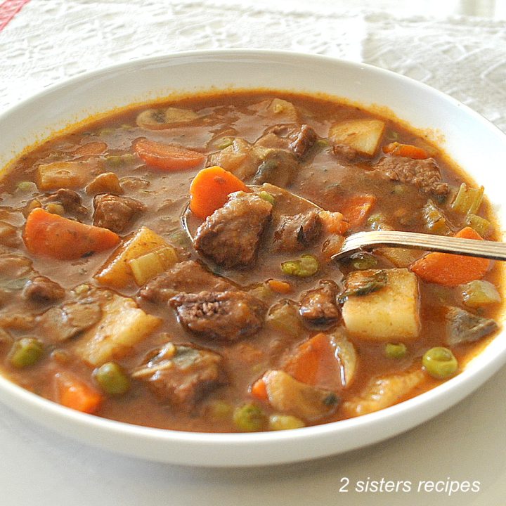 A white bowl of soup with beef chunks and vegetables, with a spoonful.