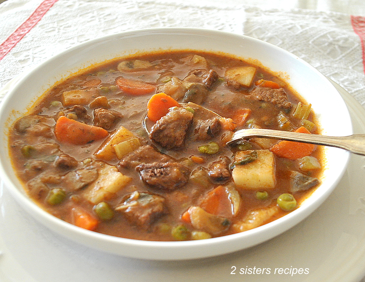 A white bowl of soup with beef chunks and vegetables, with a spoonful.