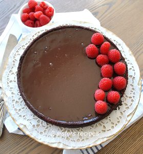 A Chocolate Cake with fresh raspberries on top set on a white cake plate.