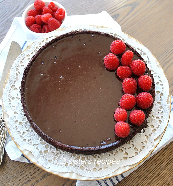 The Easiest Flourless Chocolate Cake with fresh raspberries on top on a white doily. by 2sistersrecipes.com